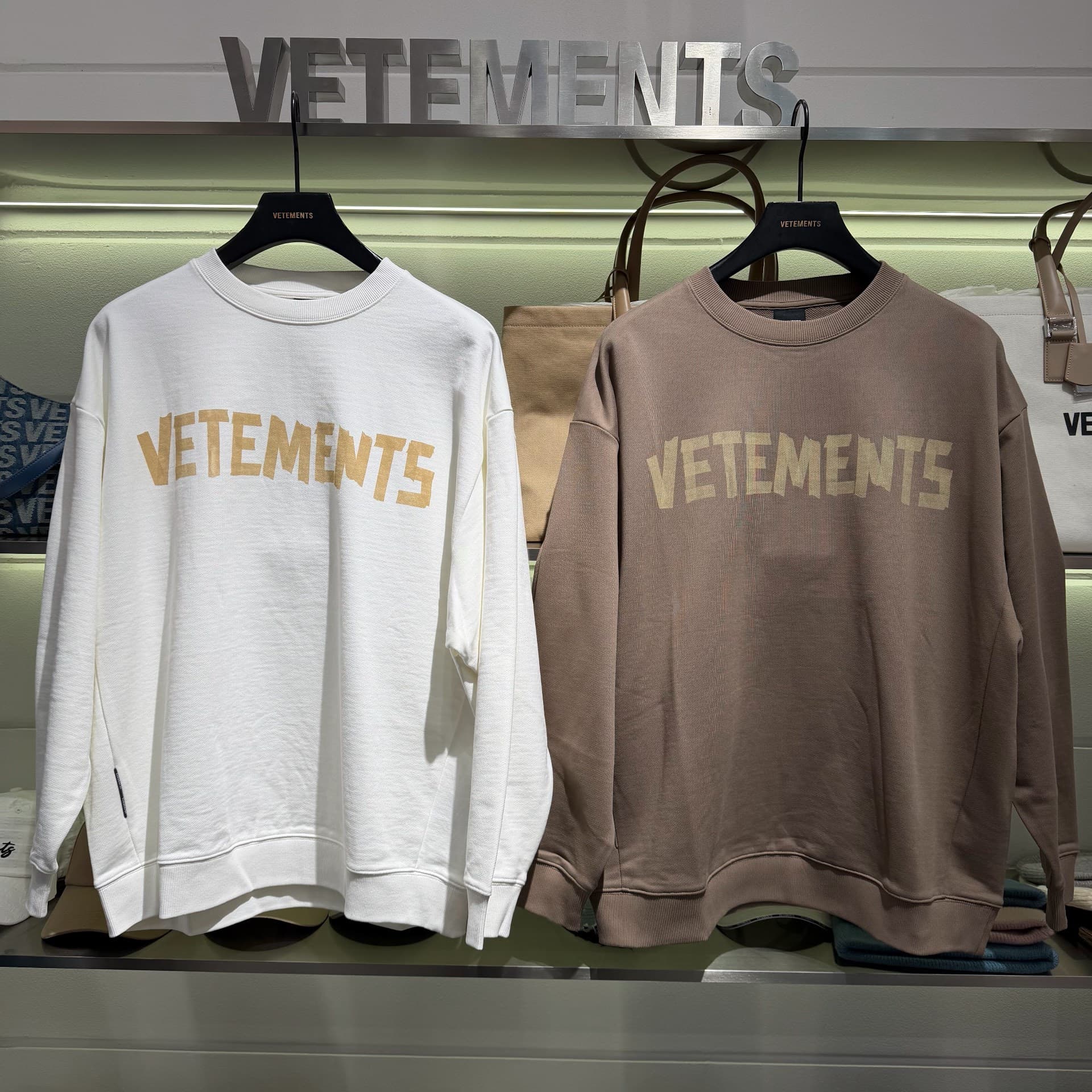 Симпатичный свитер с круглым вырезом от VETEMENTS доступен в белом и коричневом цветах.Маленькая буква "л" позади
